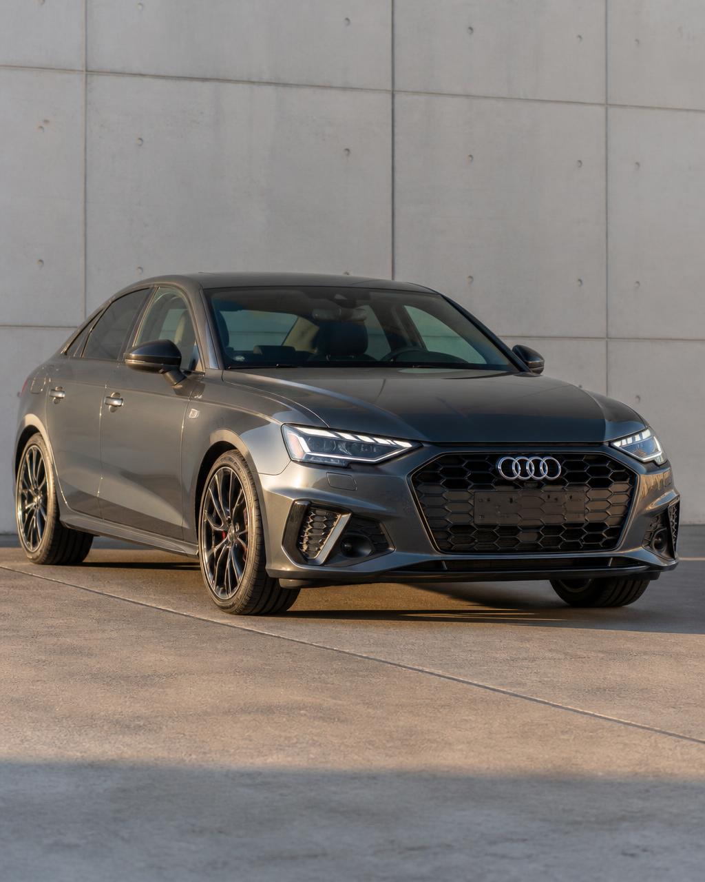 Sedã Audi cinza parado, sem placa, em frente a um muro de concreto